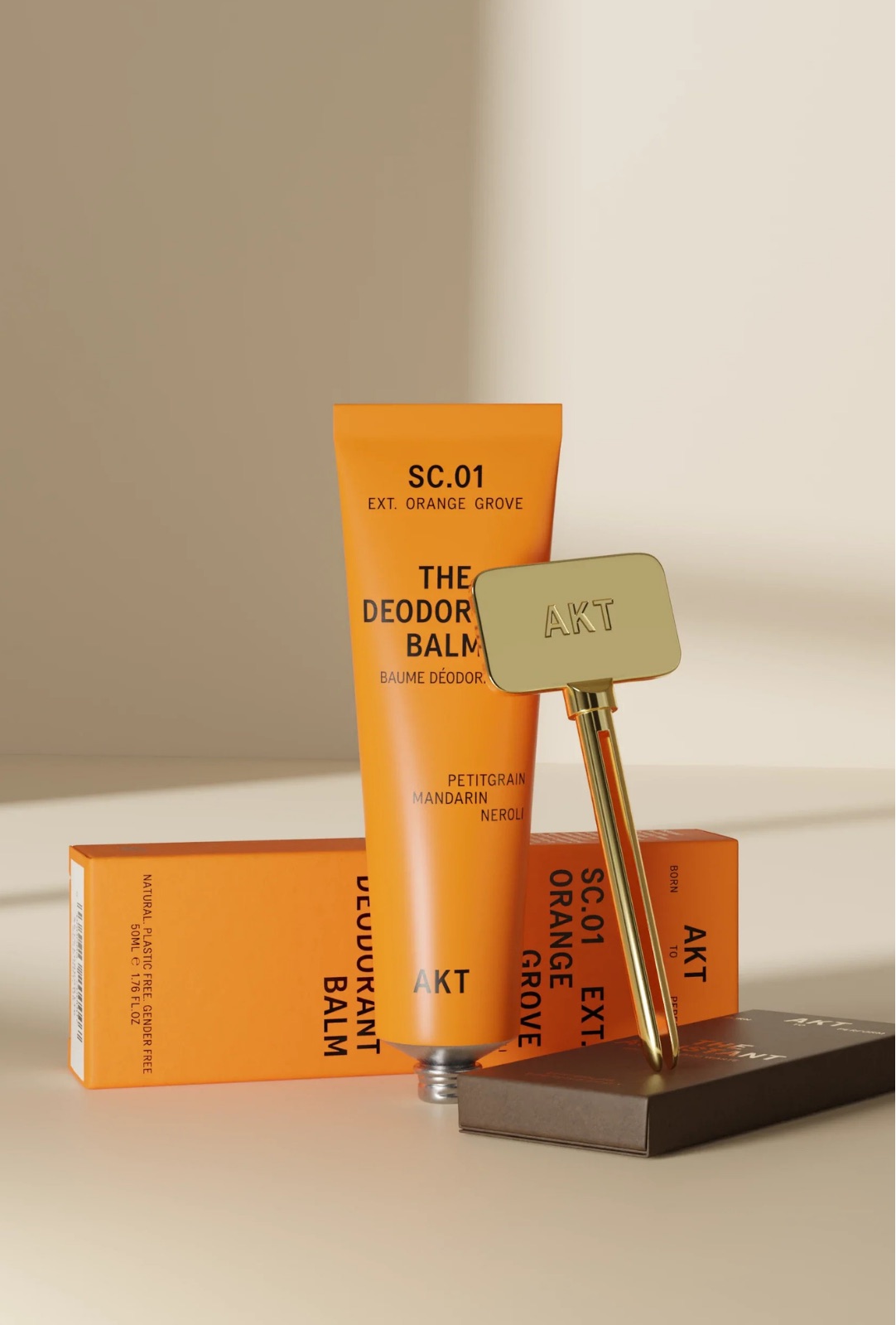 The AKT London deodorant balm tube standing with its gold applicator and orange cartons